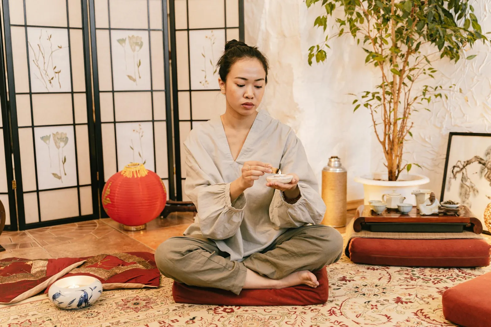 Asian woman meditating with a candle in a tranquil indoor setting, promoting relaxation and zen.
