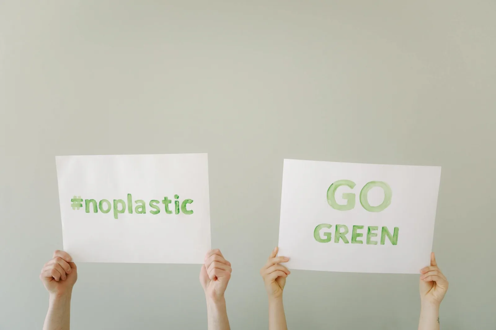 Hands holding eco-friendly signs advocating 'No Plastic' and 'Go Green'. Environmental awareness concept.