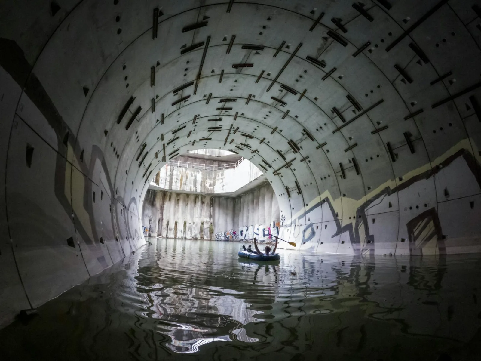 Inflatable boat paddles through a graffiti-covered tunnel filled with water, showcasing urban exploration.