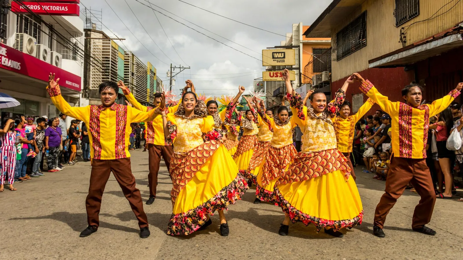 A lively street parade with dancers in bright yellow and orange costumes, celebrating a cultural festival.