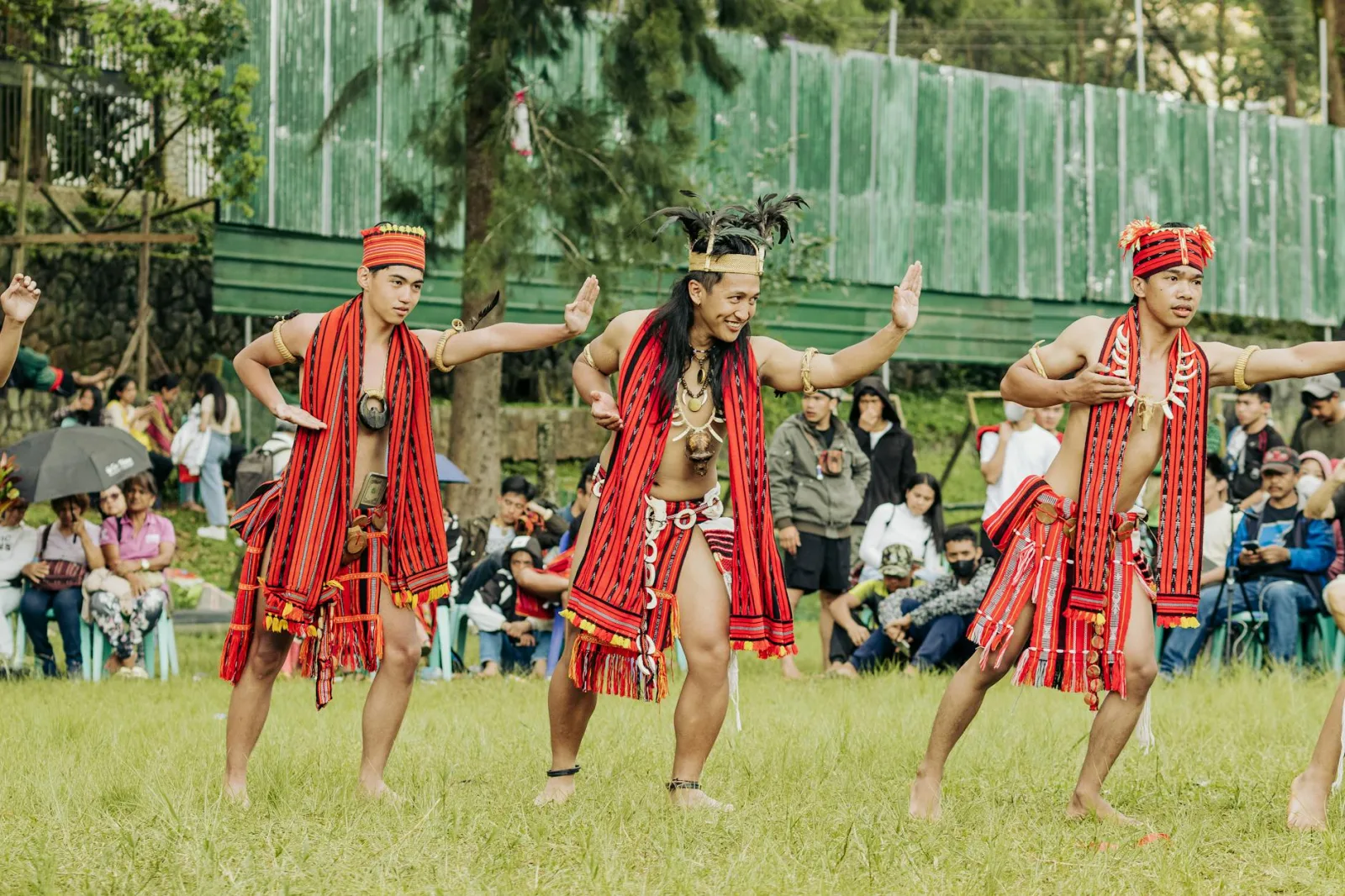 Men in traditional clothing perform a cultural dance at an outdoor event.