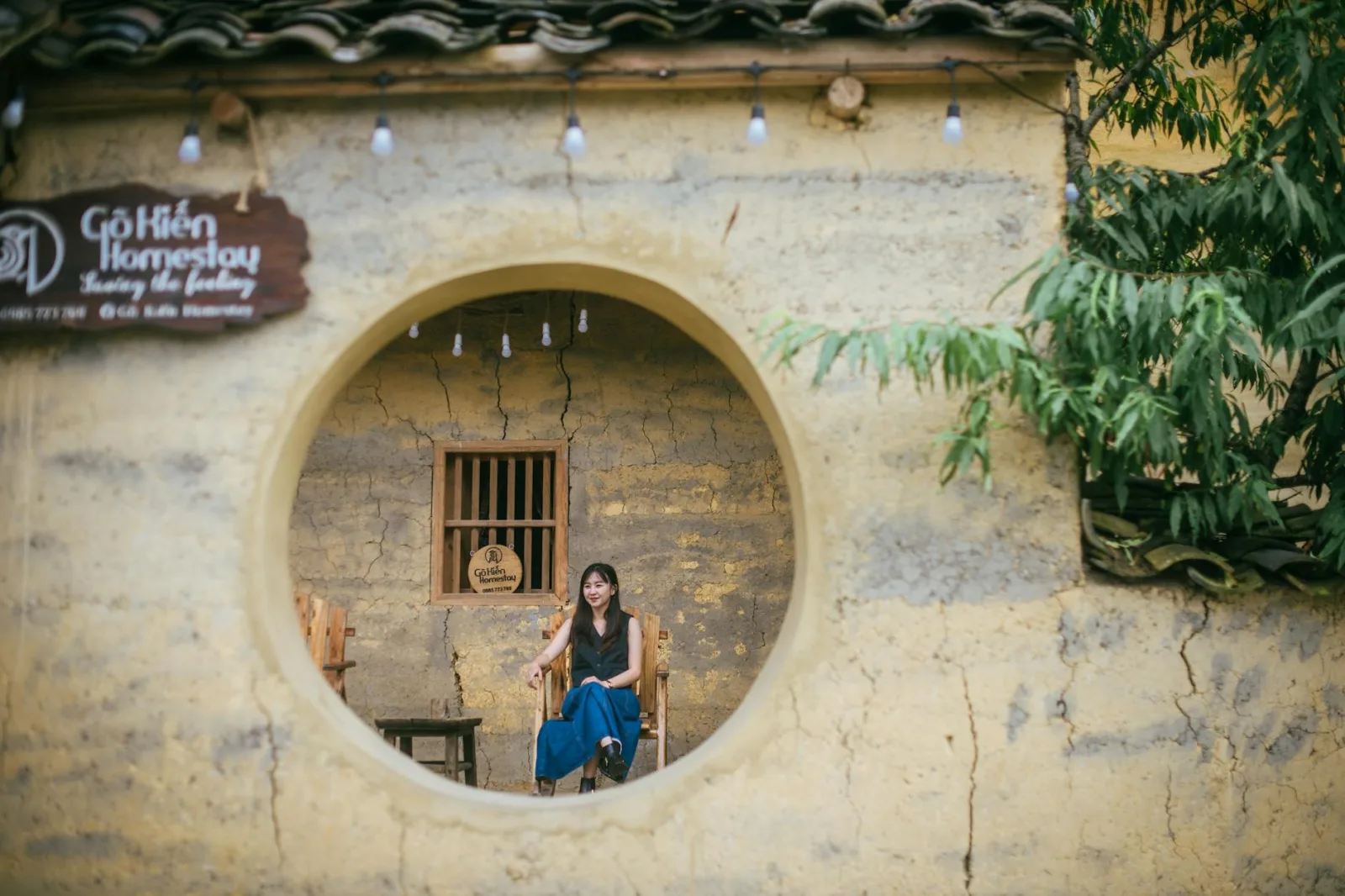 A woman seated in a rustic homestay capturing the essence of traditional architecture.