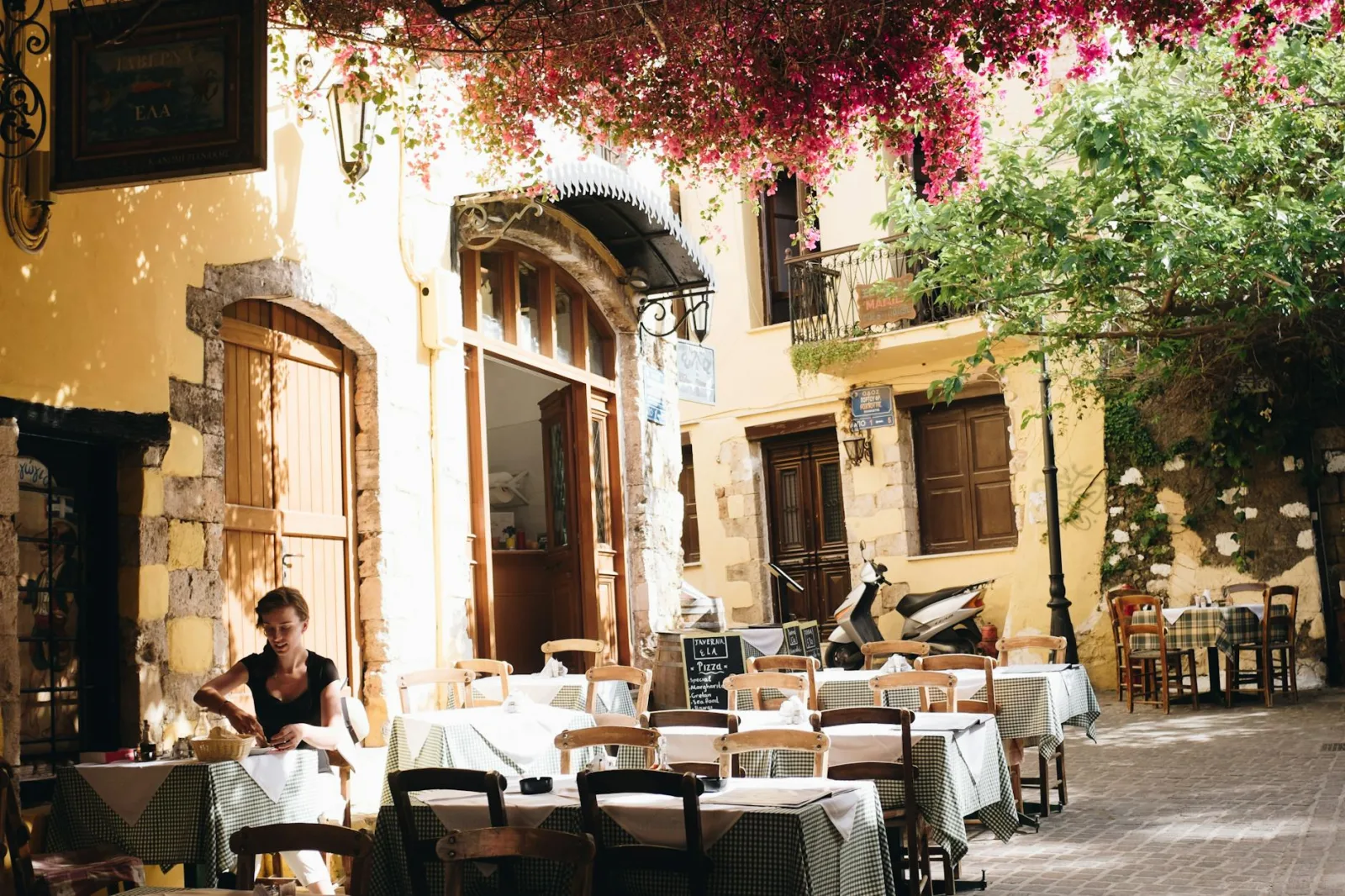 A quiet outdoor cafe in Chania, Greece, under sunlight and vibrant flowers.