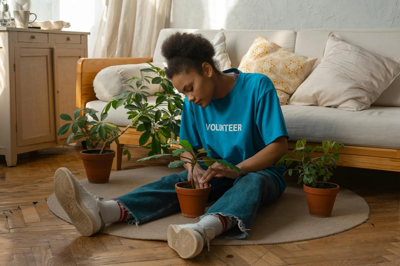 A woman in a blue volunteer shirt tending to potted plants on a wooden floor.