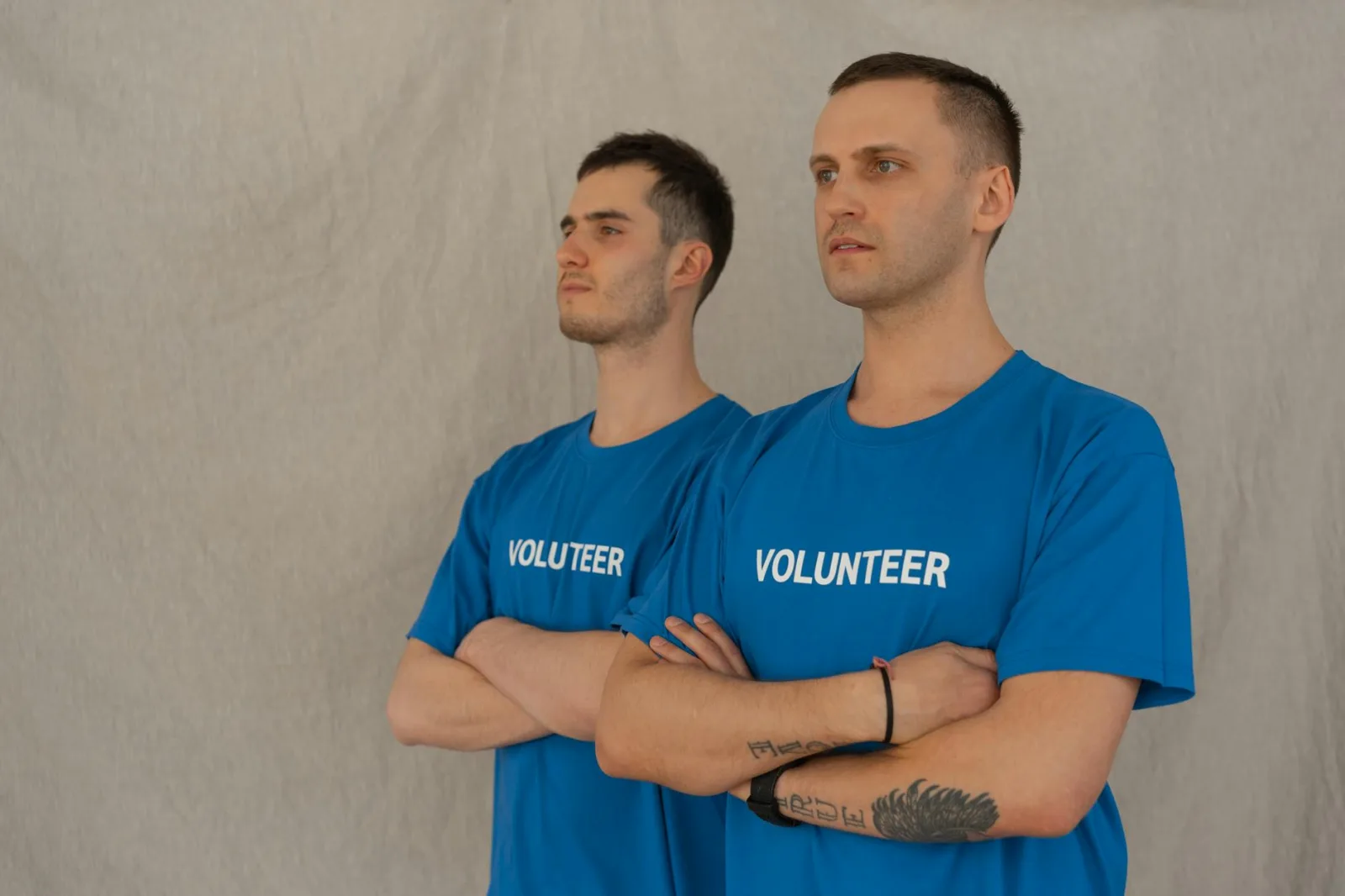 Two men in blue volunteer shirts standing with arms crossed, showing unity and support.