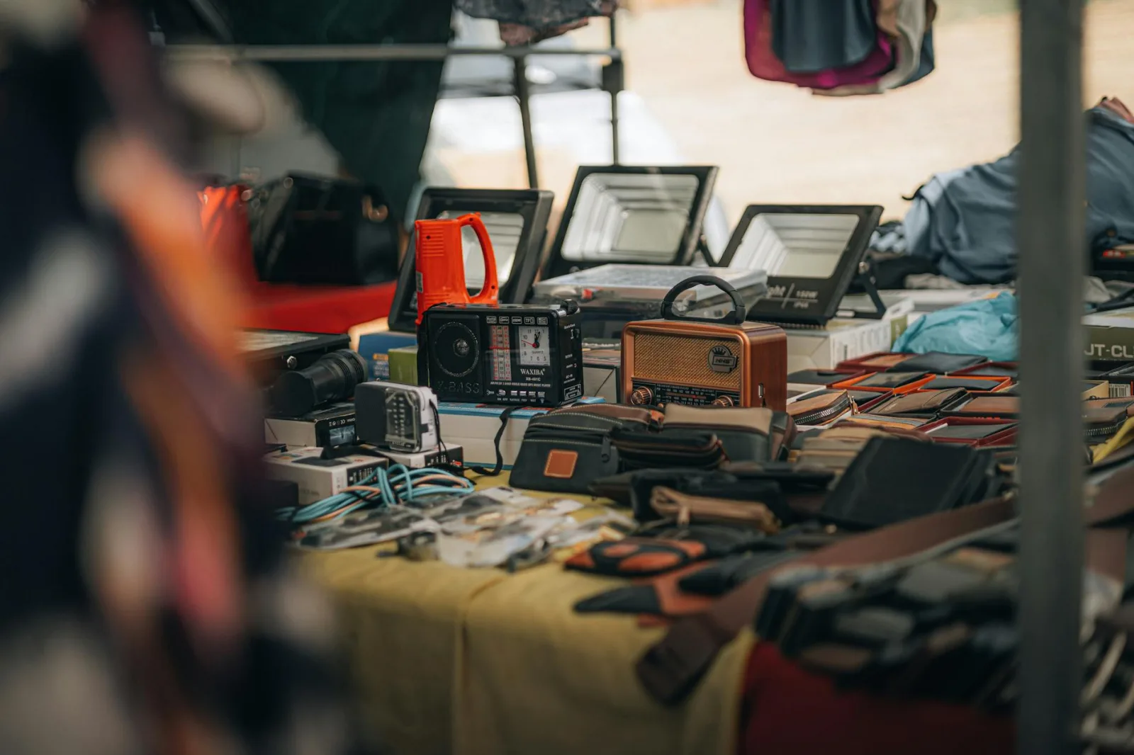 A tabletop display of vintage radios, gadgets, and leather goods at an outdoor flea market.