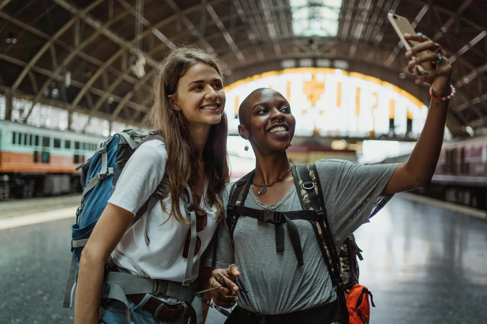 Two young women take a selfie while waiting at a railway station, capturing their travel adventure.