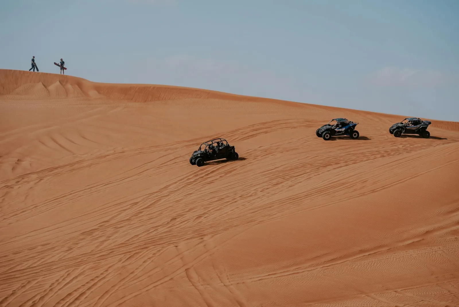 Exciting off-road adventure with vehicles navigating stunning desert dunes under a clear sky.