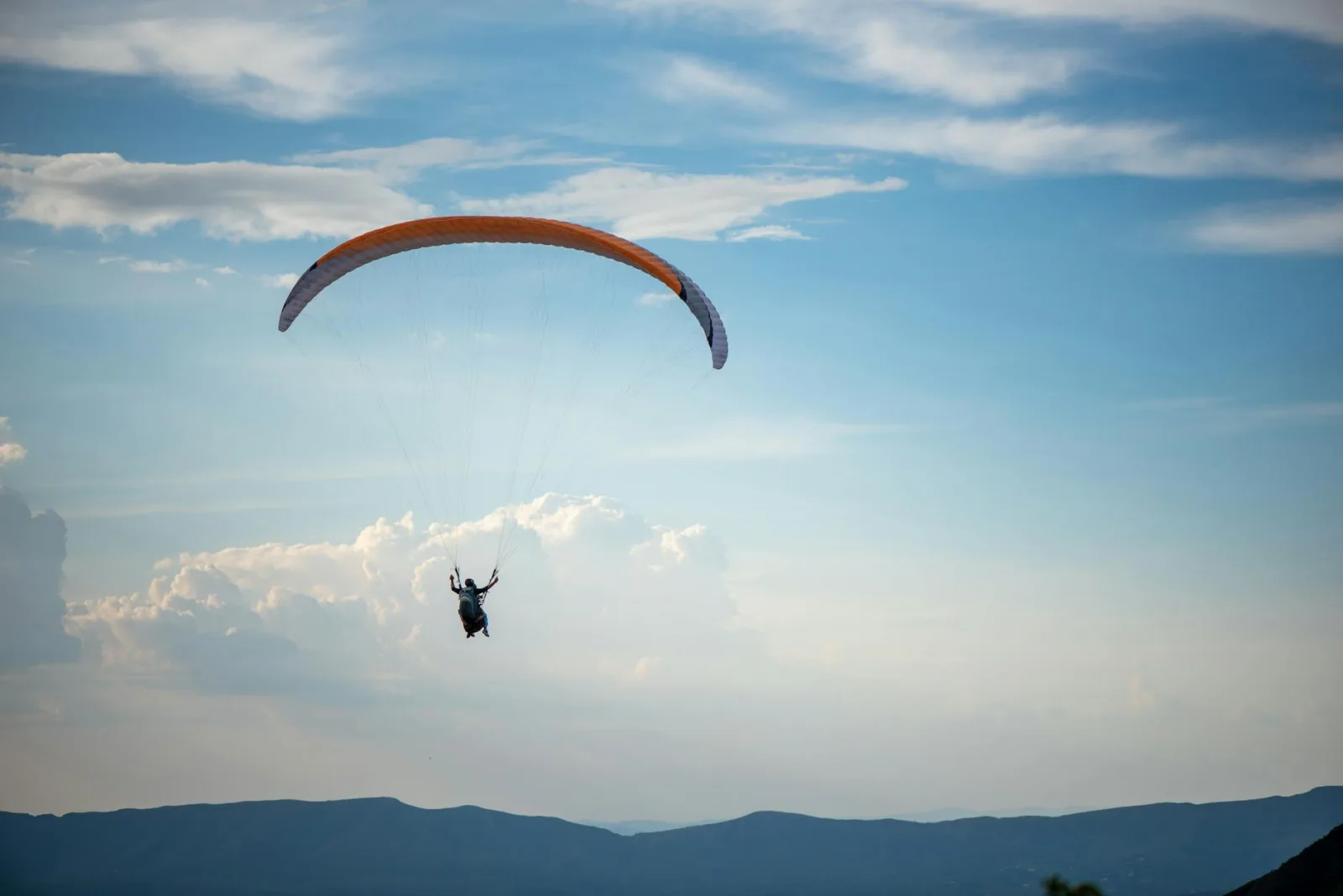 Enjoy the thrill of paragliding over Belo Horizonte with breathtaking mountain views in a clear blue sky.