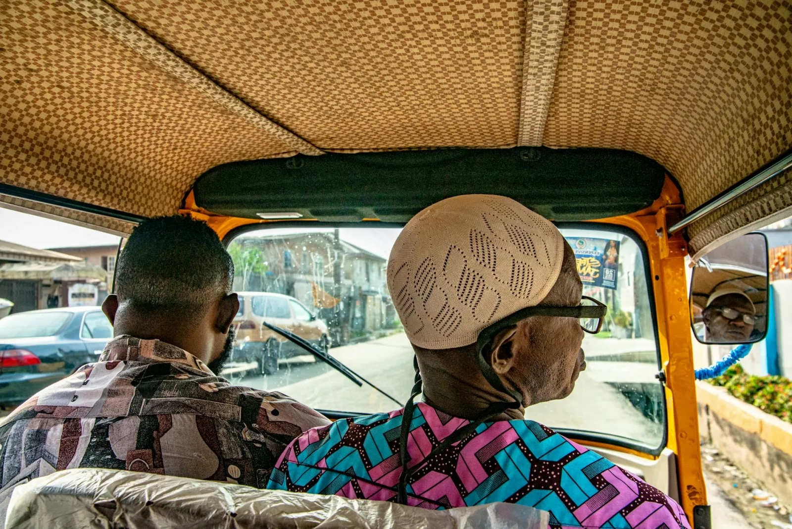 Two men sitting inside a vibrant rickshaw on a sunny day in the city.