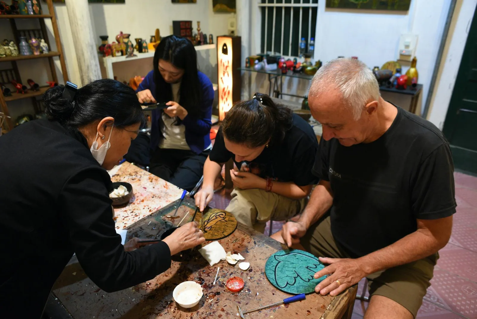 Adults engaged in a hands-on crafting workshop, learning lacquer techniques in a cozy studio.