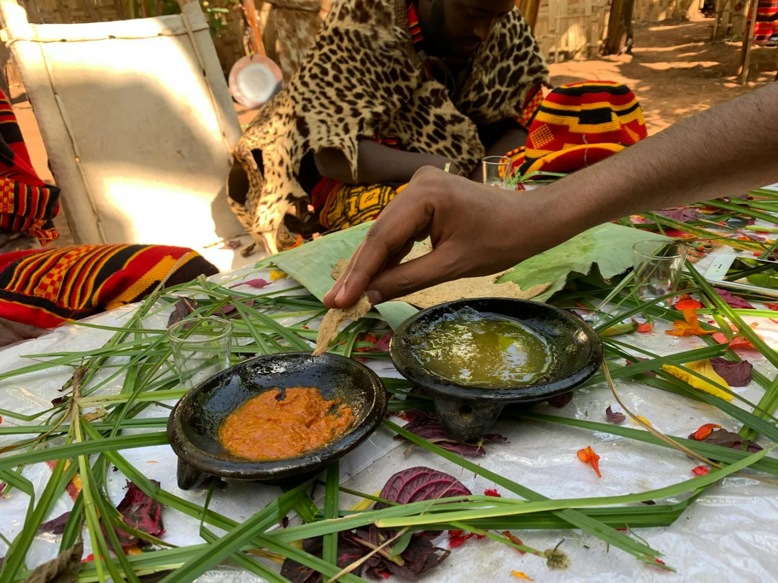 Hand preparing African dish with two sauces amid colorful traditional textiles.
