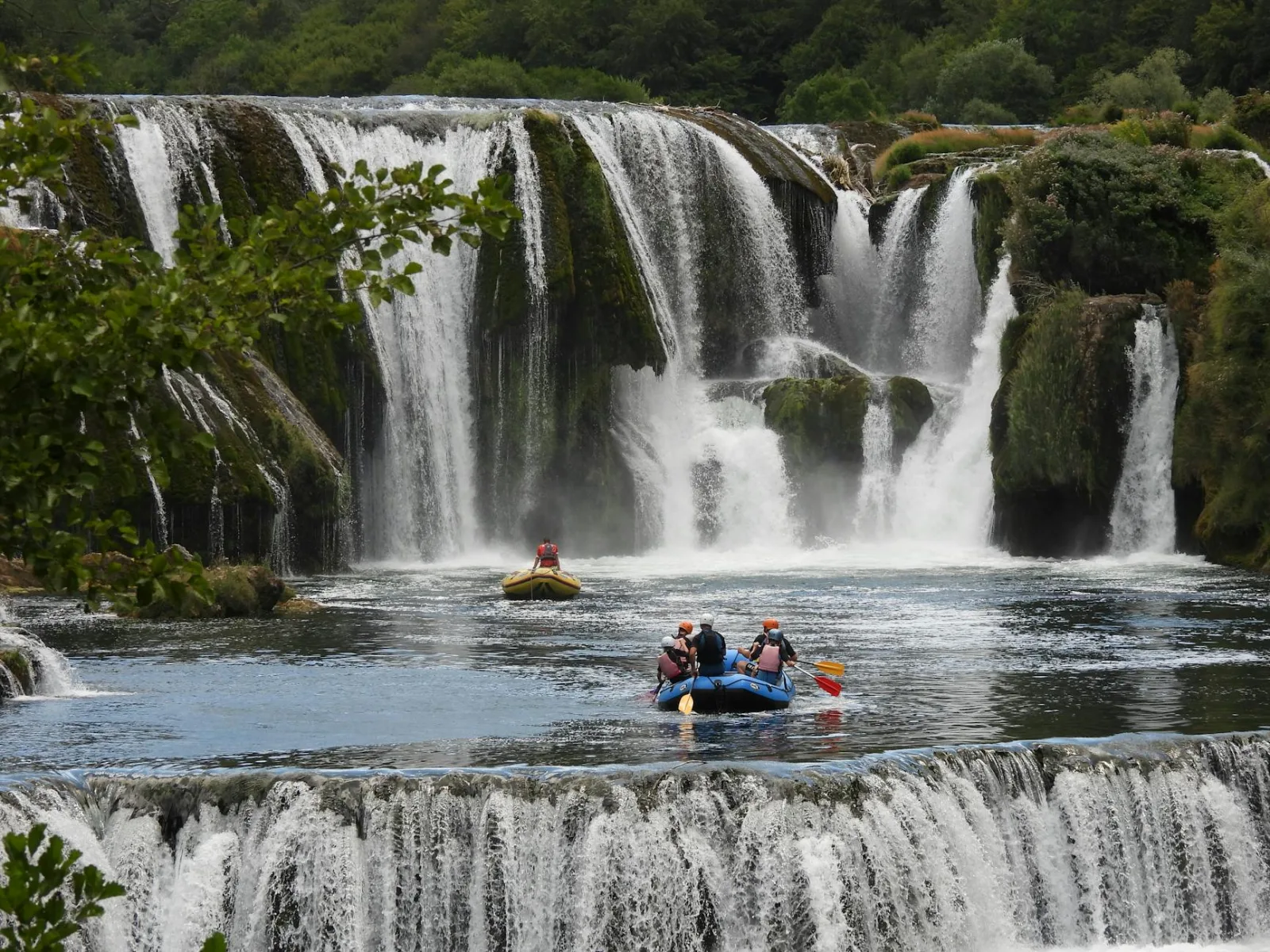 Experience the excitement of rafting near majestic cascading waterfalls surrounded by lush nature.