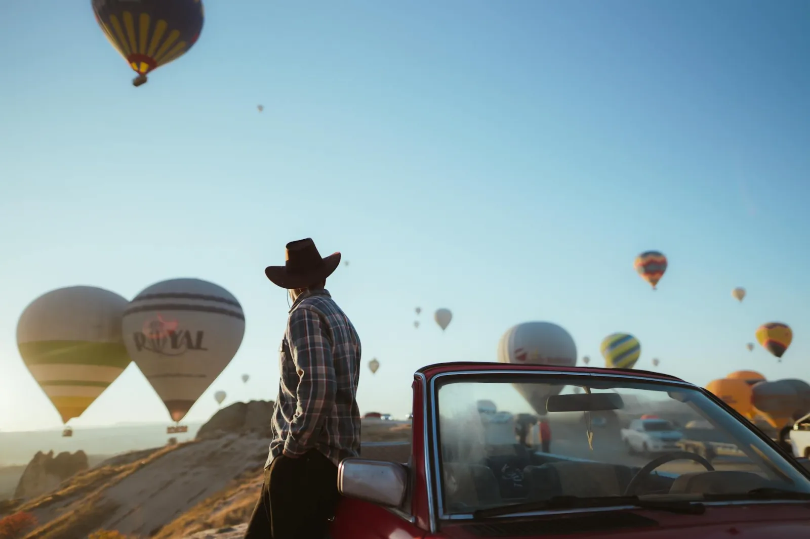 Man enjoying hot air balloons at sunrise in Cappadocia, Turkey, with clear skies and scenic views.