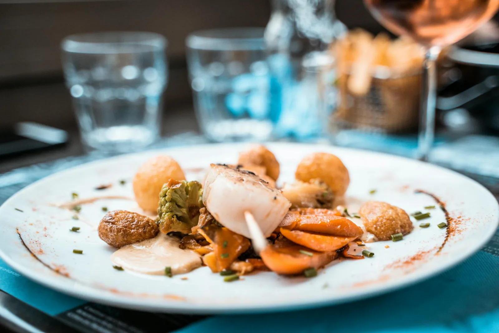Beautifully plated scallop dish with vegetables and fries in a French restaurant setting.