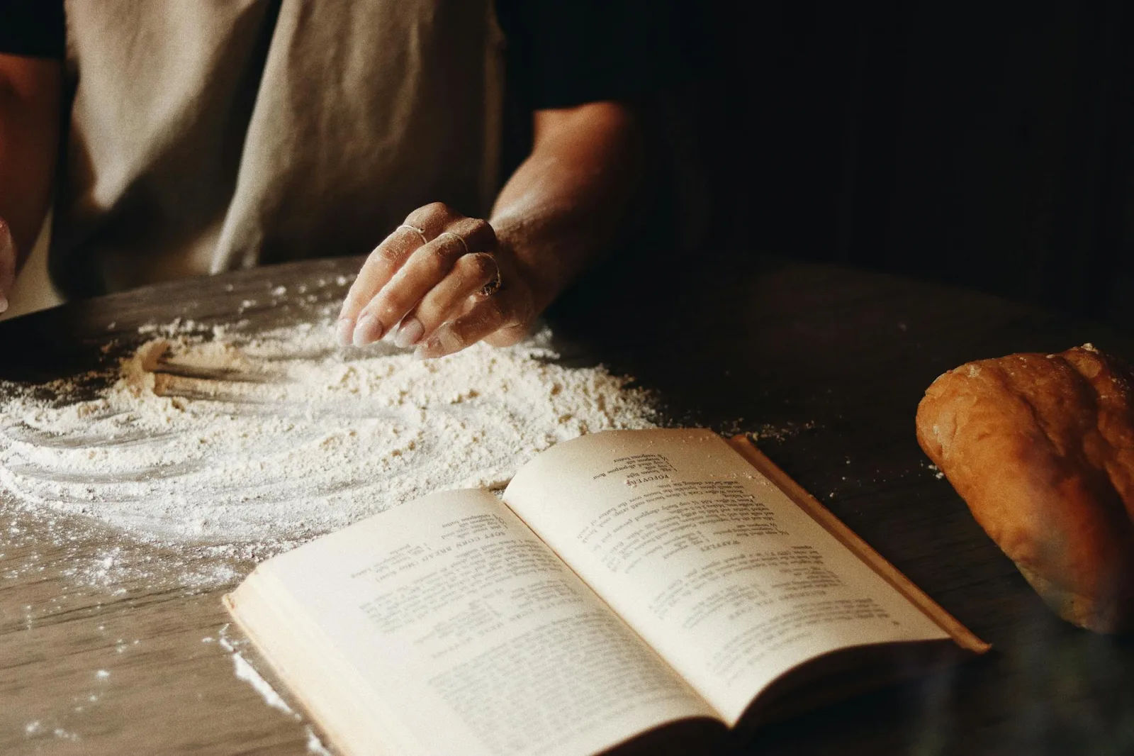 A close-up of hands shaping dough beside an open recipe book, capturing the art of home baking.