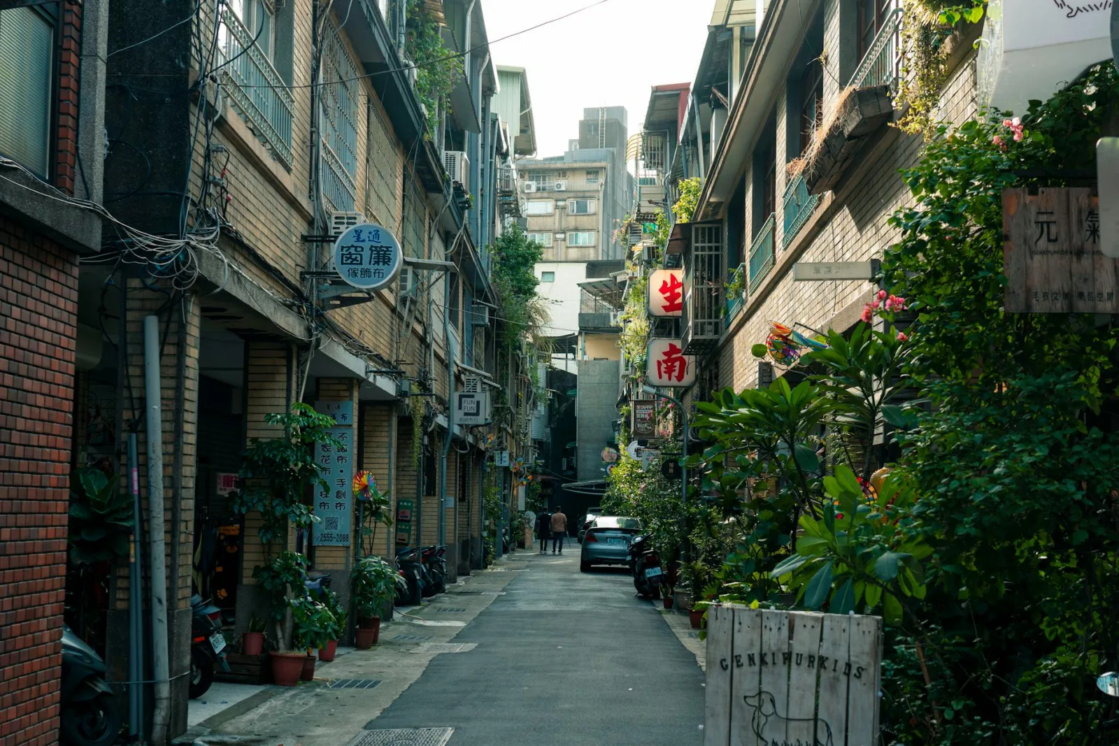Explore a narrow alley in an Asian city with lush plants and atmospheric street signs.