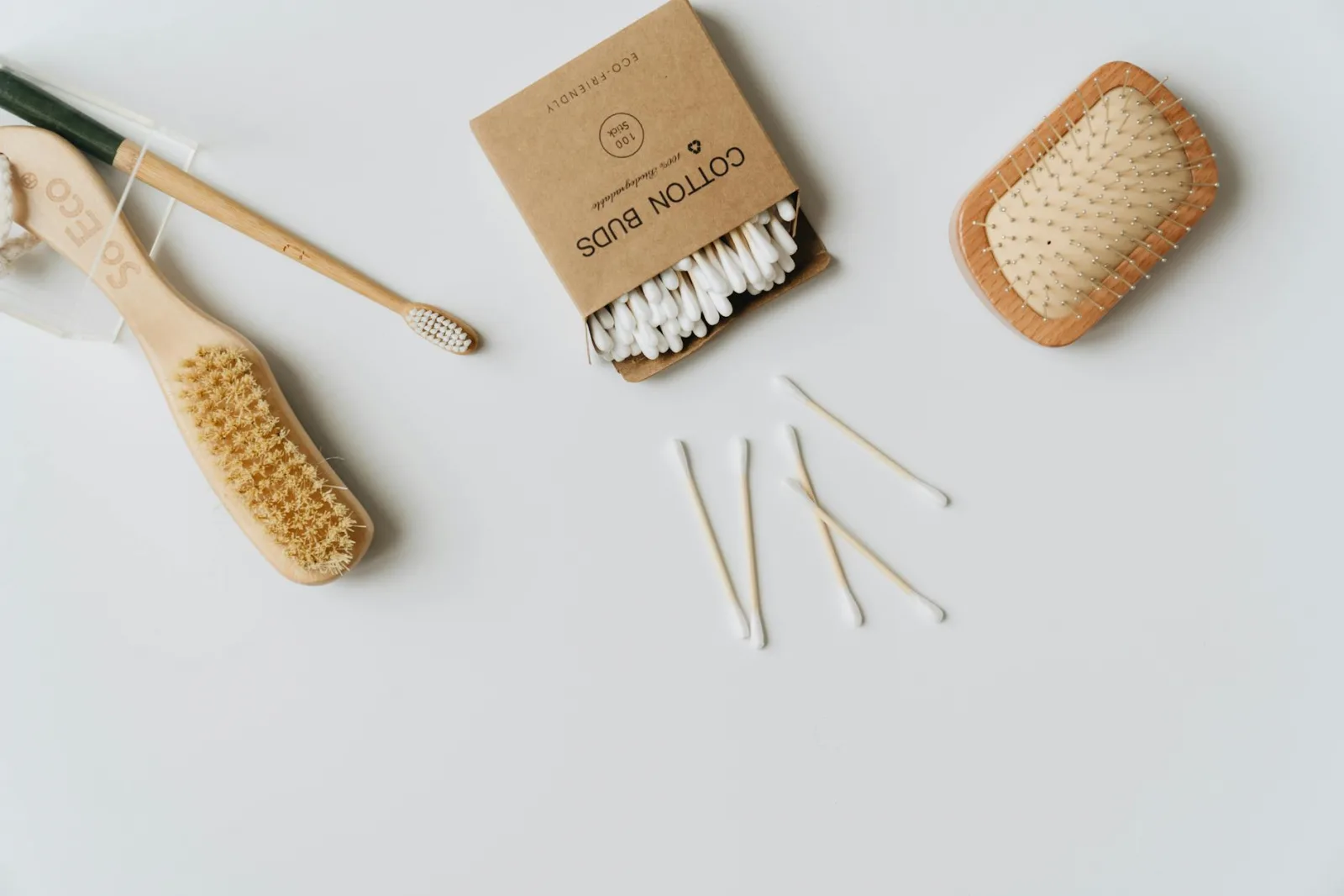 Minimalist flat lay of eco-friendly personal care items including a toothbrush, hairbrush, and cotton buds on a white background.