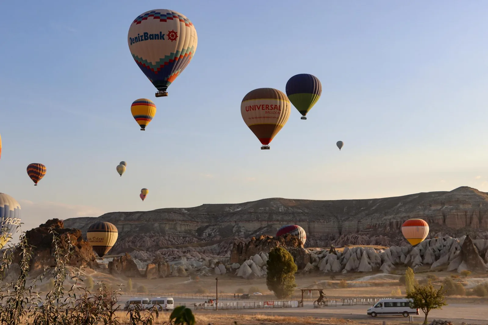 Hot air balloons flying over the rocky terrain of Cappadocia at sunrise.