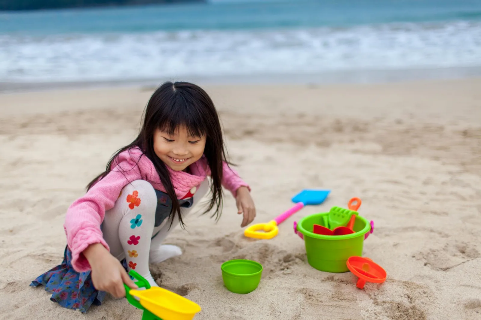 A young girl enjoys a day at the beach playing with colorful toys by the sea in Hong Kong.