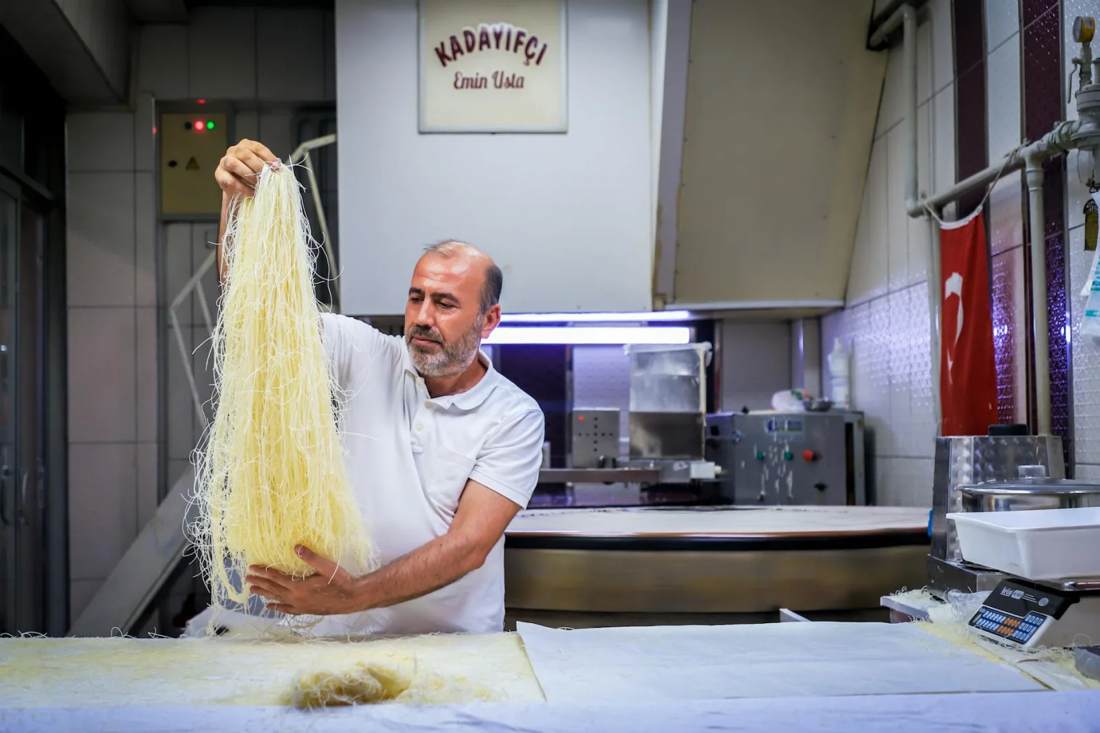 Chef in white shirt preparing traditional Turkish kataifi dessert in a restaurant kitchen.