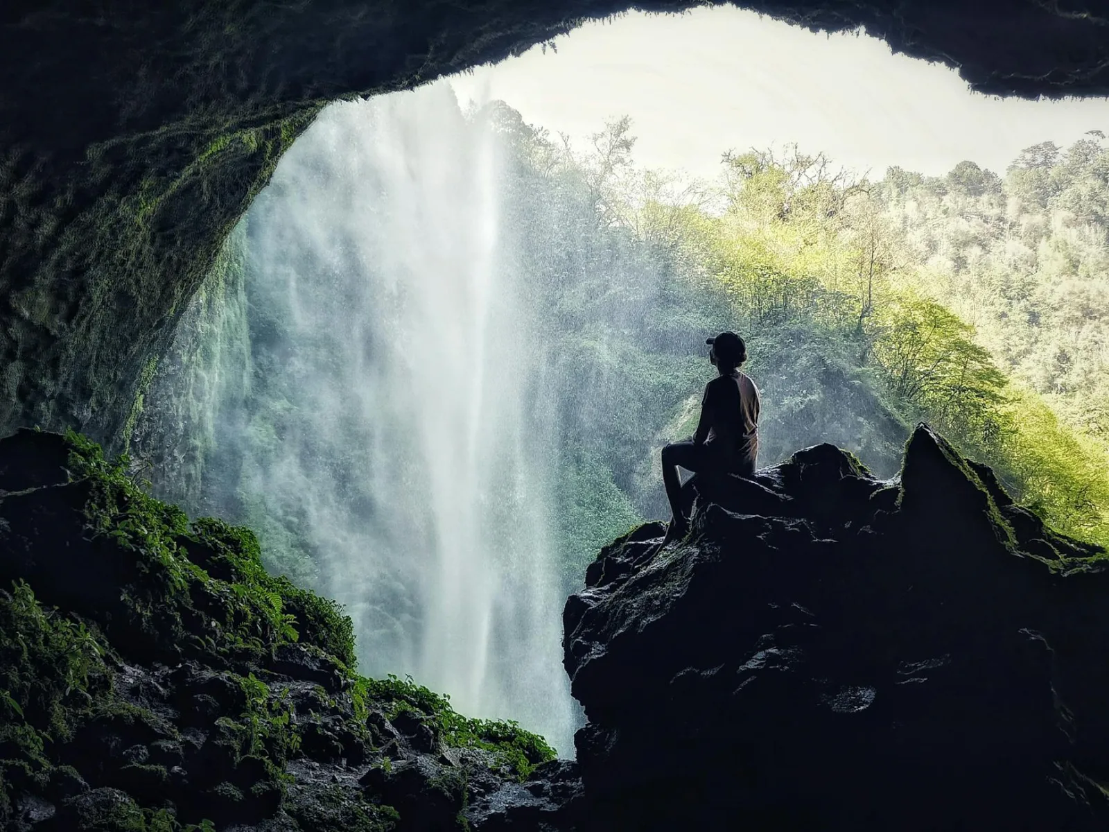 Silhouette of a person exploring a lush waterfall cave in Mexico's natural beauty.