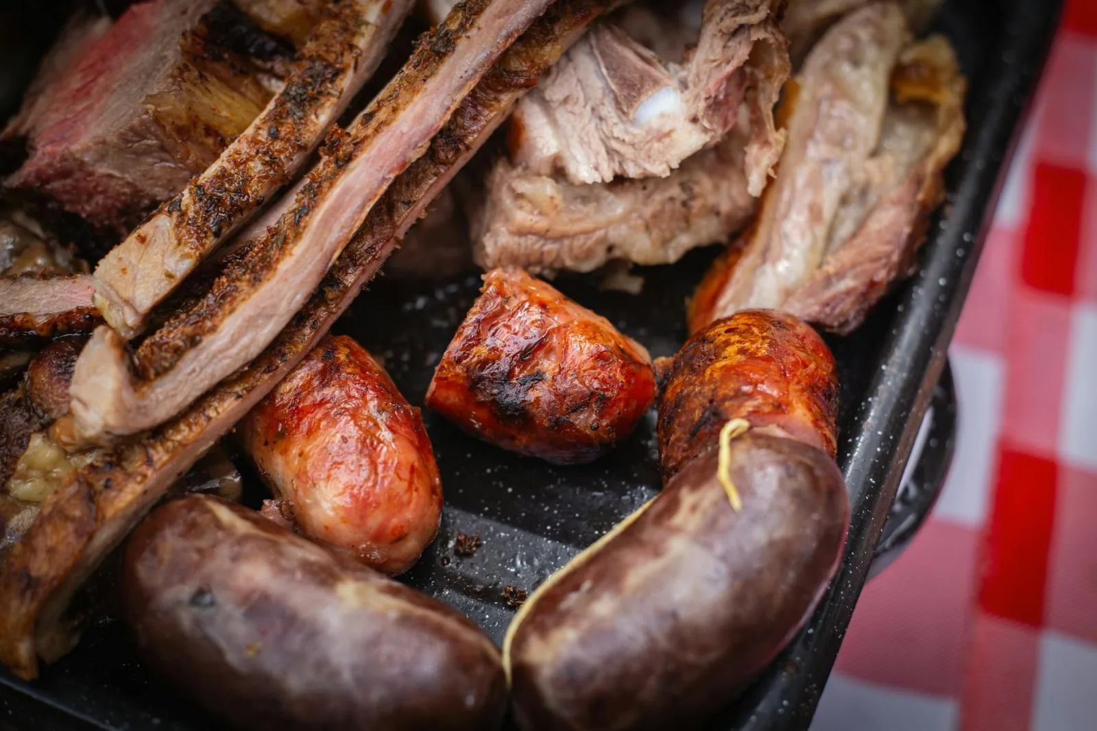 A close-up of Argentine asado with grilled ribs and sausages on a black grill tray.