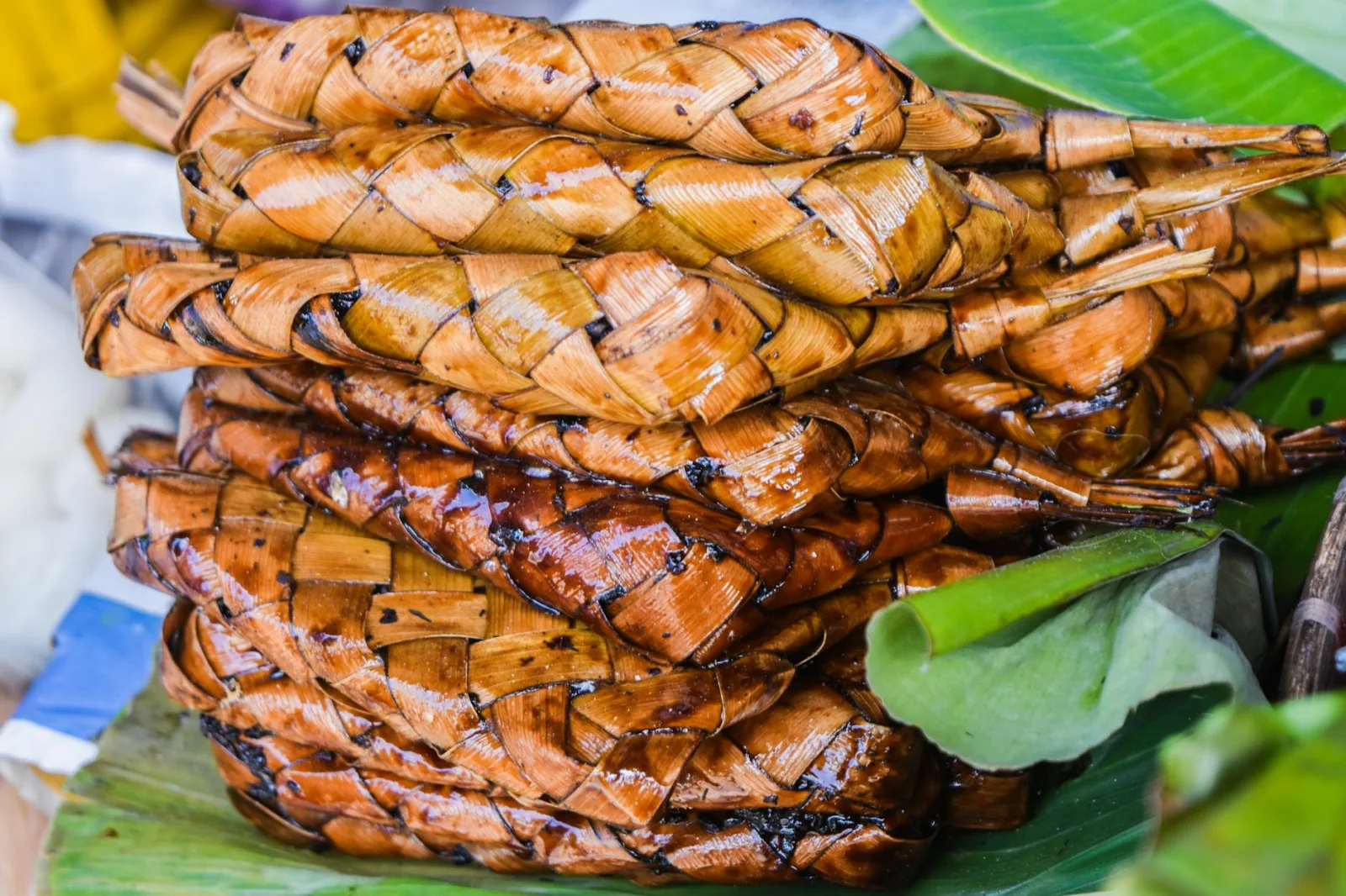 Stack of grilled suman wrapped in woven palm leaves, a Filipino delicacy.