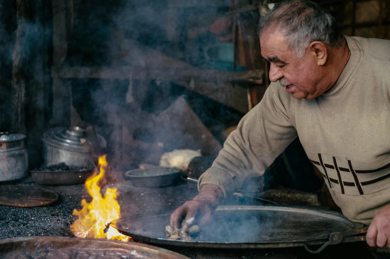 Senior man cooking with pots over an open flame in Denizli, Türkiye.