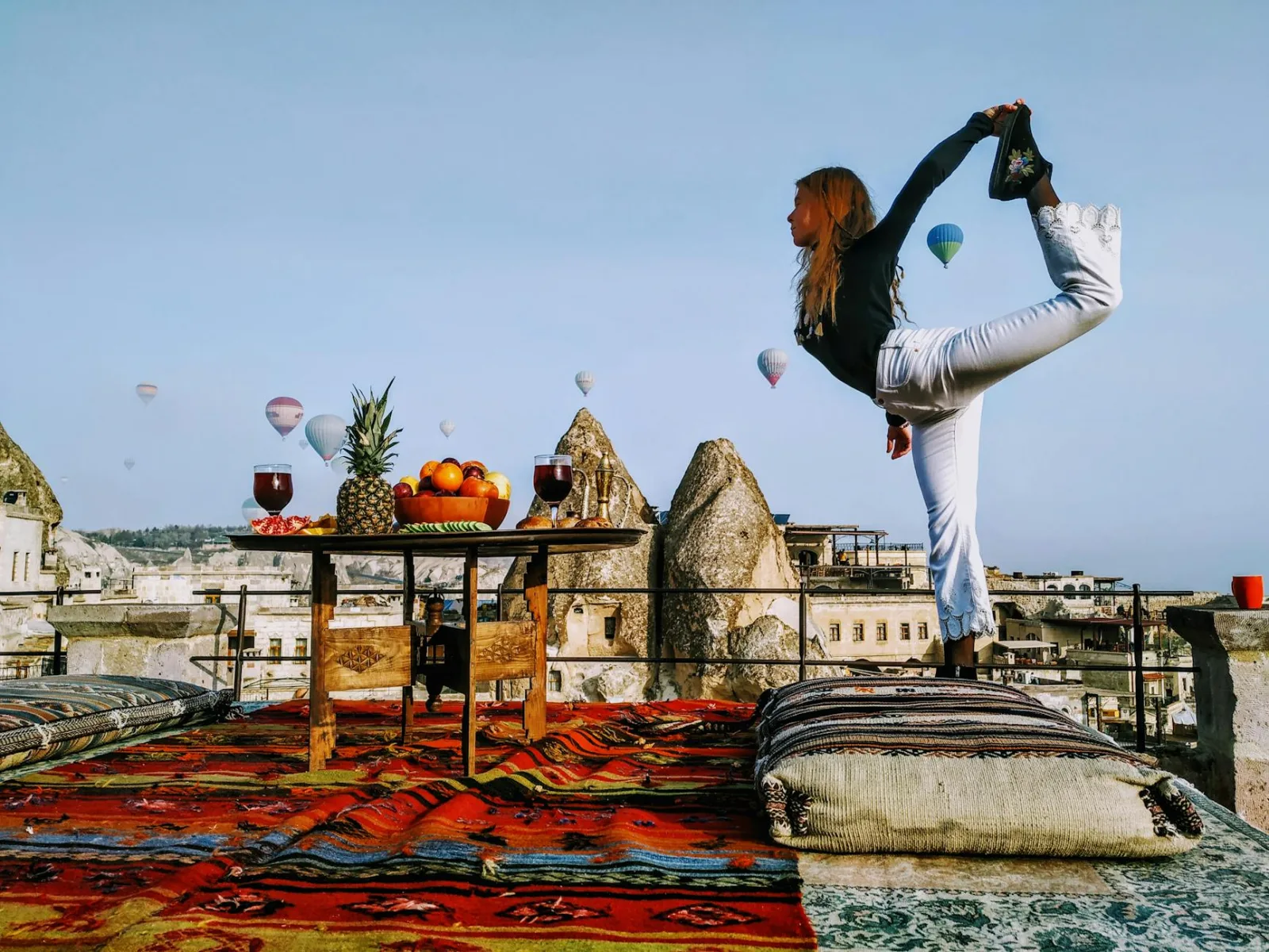 Woman performing yoga on a colorful Turkish rooftop, surrounded by hot air balloons in Cappadocia.