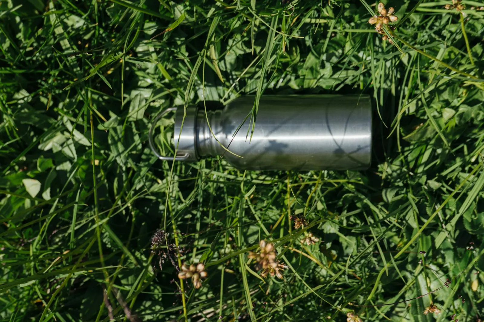 Close-up of a stainless steel tumbler lying on lush green grass, bright daylight.