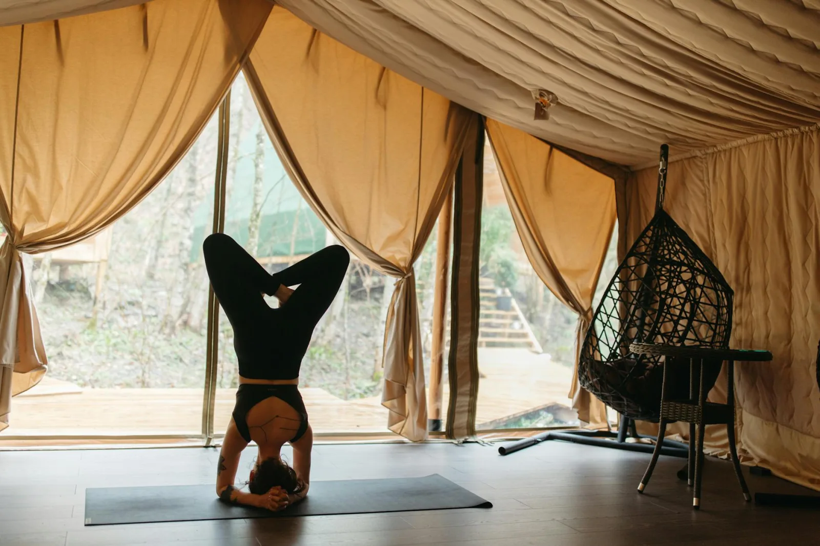Woman performing yoga headstand in a tranquil glamping tent with nature views.