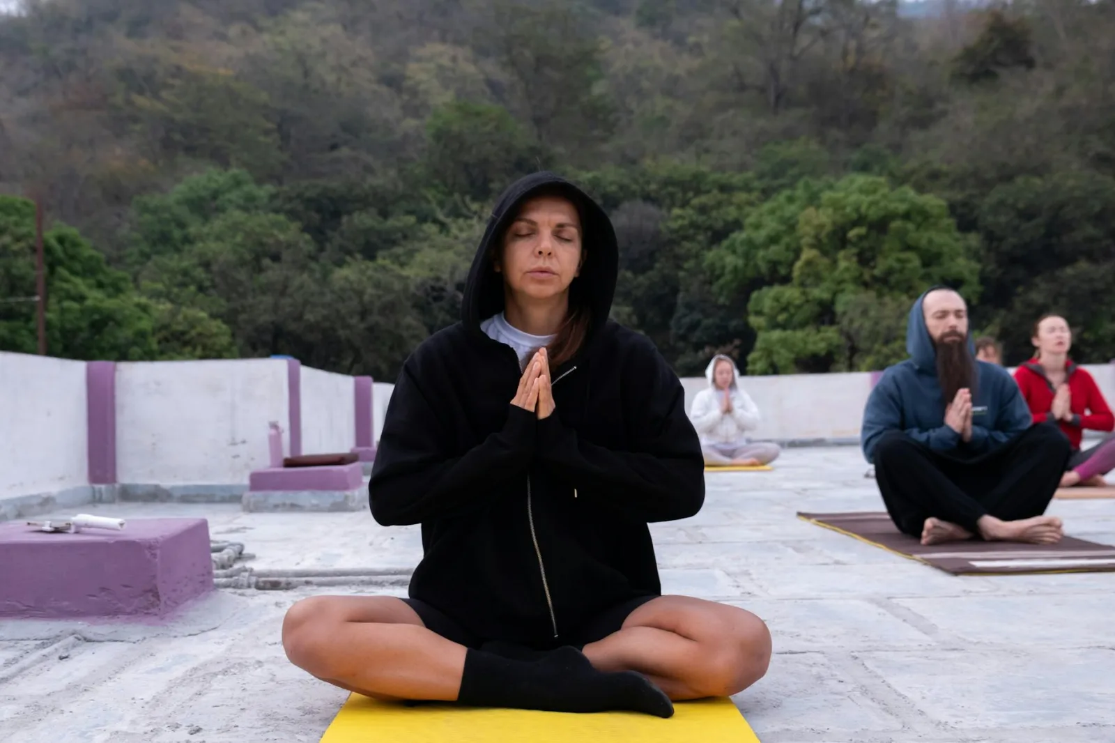 Group meditation session on a rooftop surrounded by nature, focused and calm atmosphere.