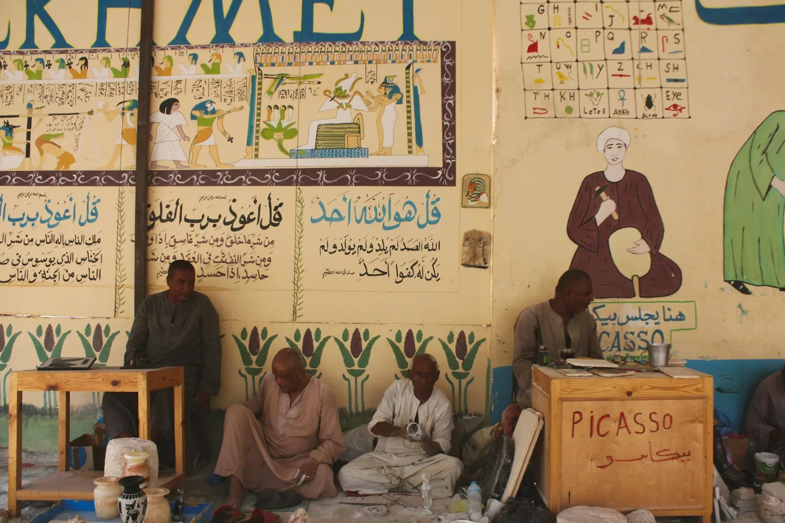 Artisans working with traditional tools in Aswan, with vibrant wall art depicting ancient Egyptian themes.