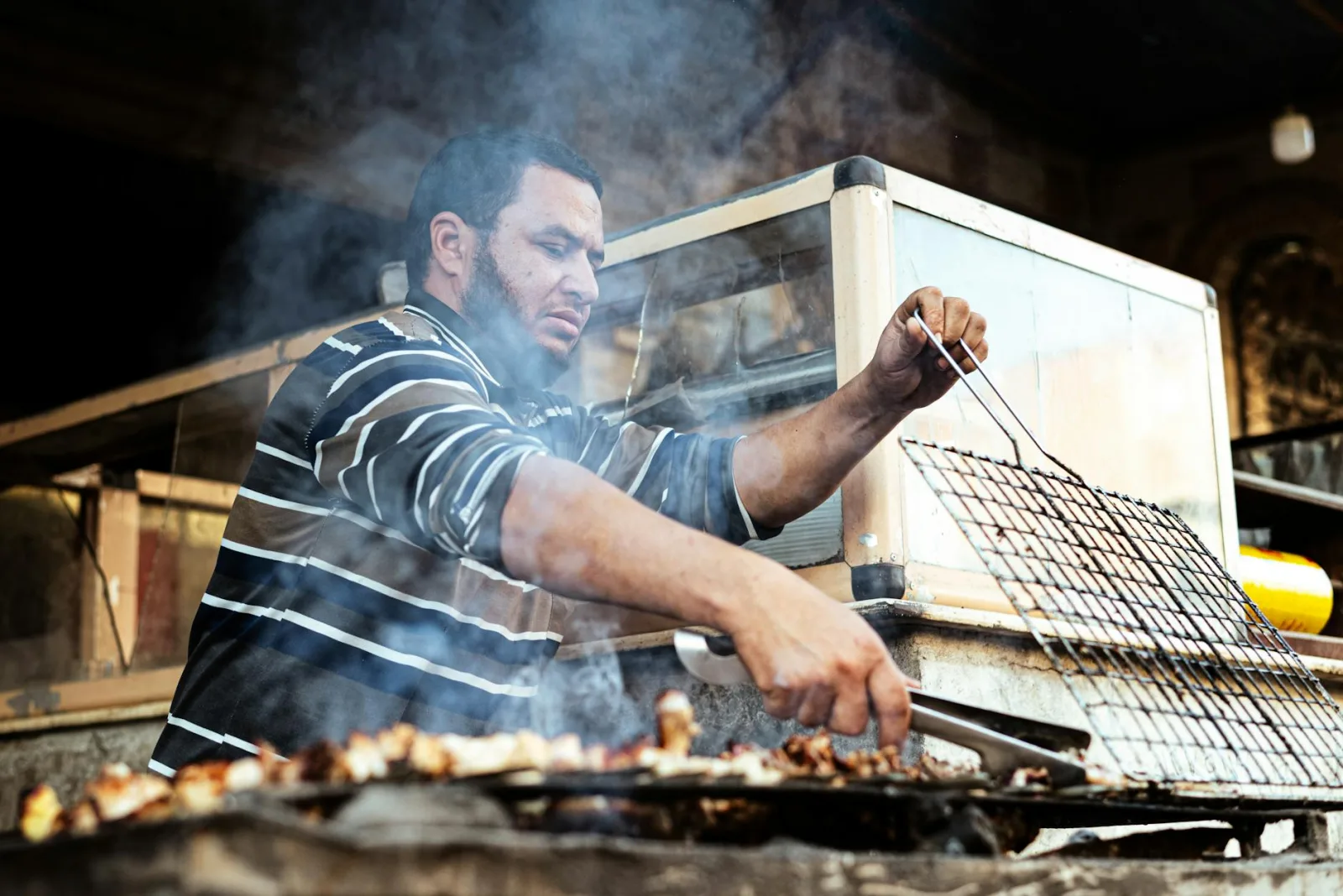 A street vendor grills meat outdoors at a bustling market stall in Egypt, showcasing local culinary culture.