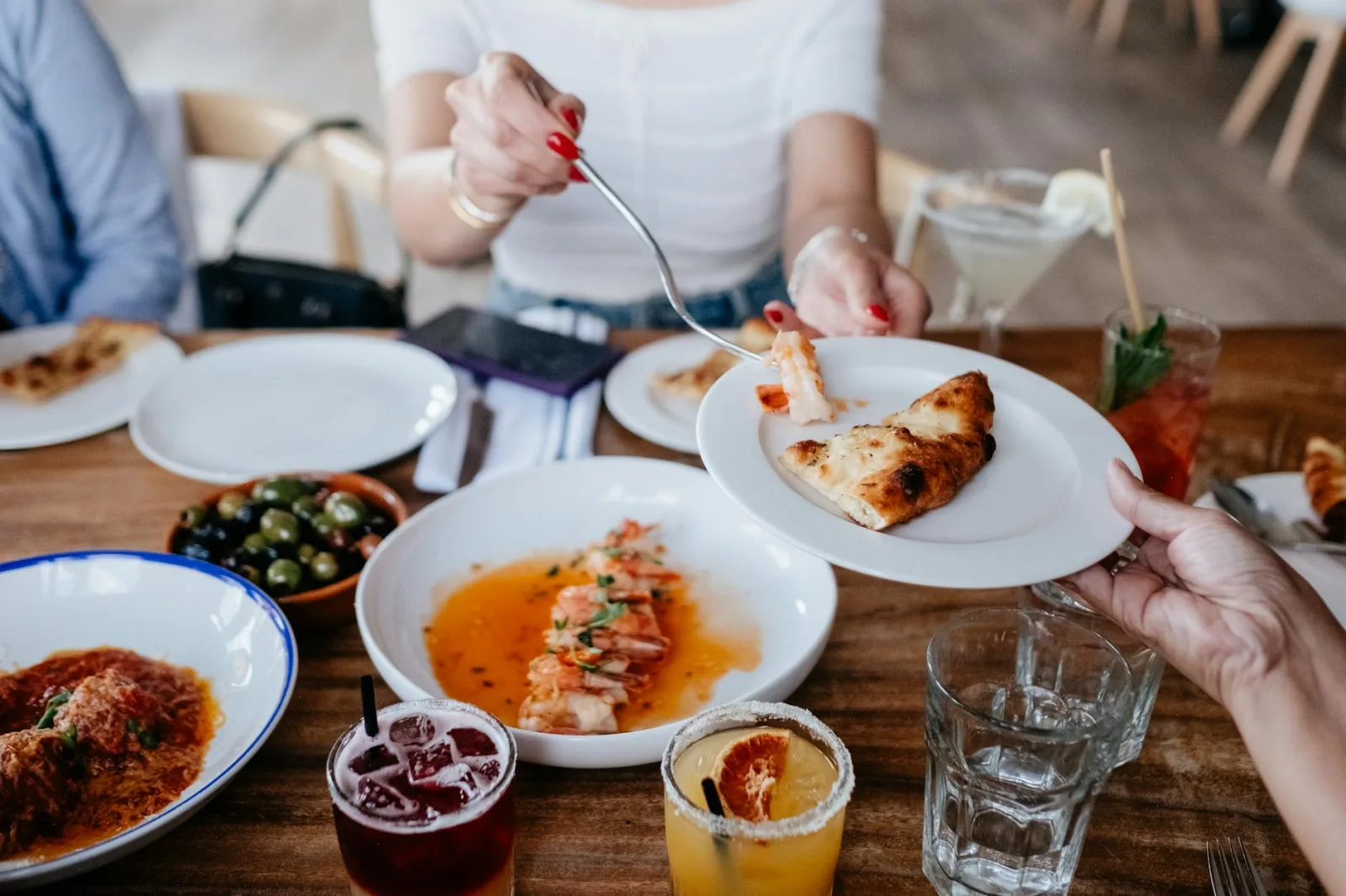 Friends enjoying a casual meal sharing various dishes and drinks at a restaurant.