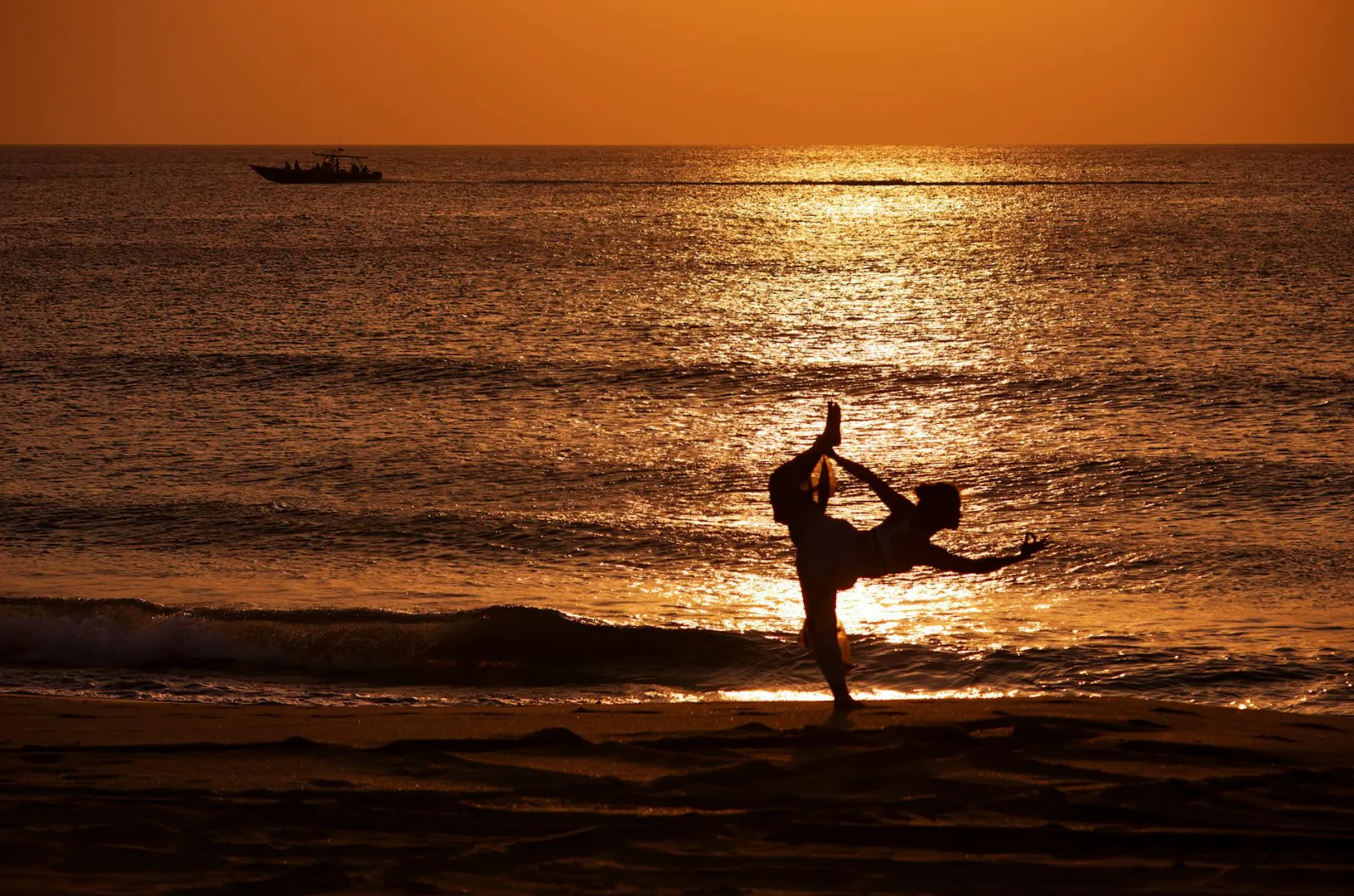 A woman practices yoga in a striking silhouette against a sunset on Fujairah's coastline.