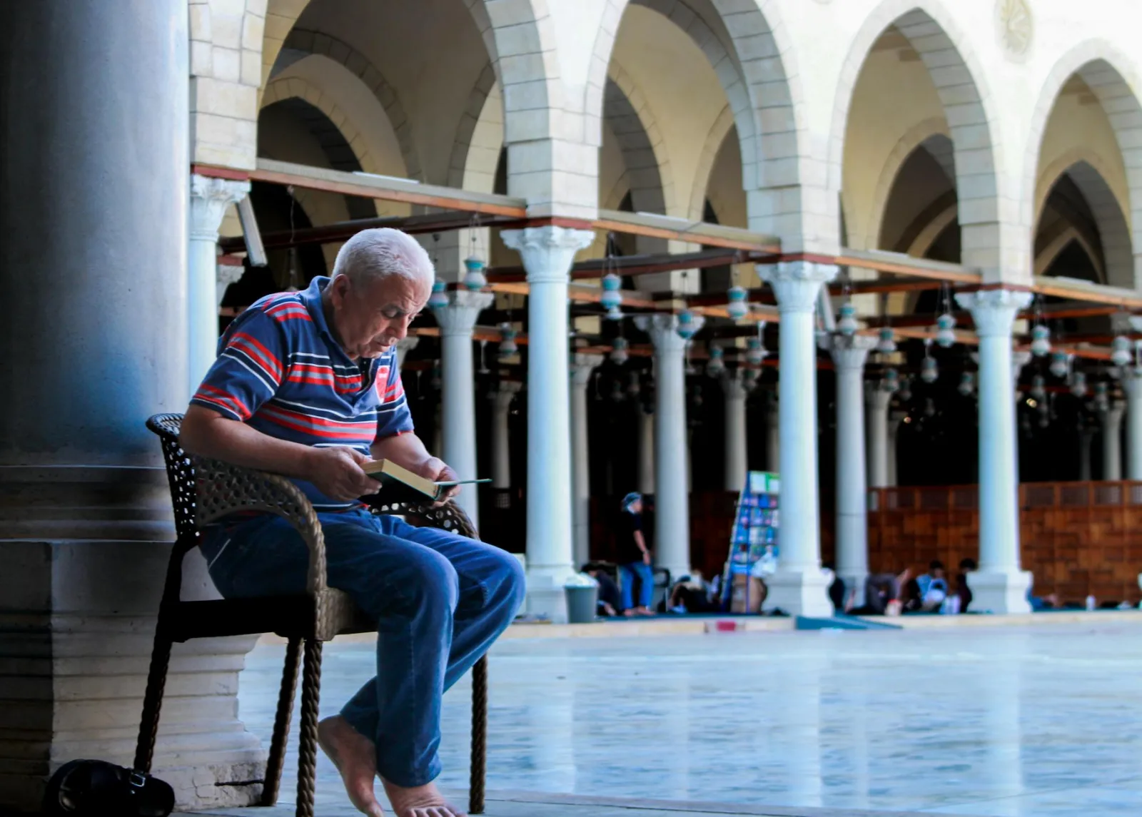 An elderly man reads in a historic Cairo mosque, reflecting serenity and tradition.