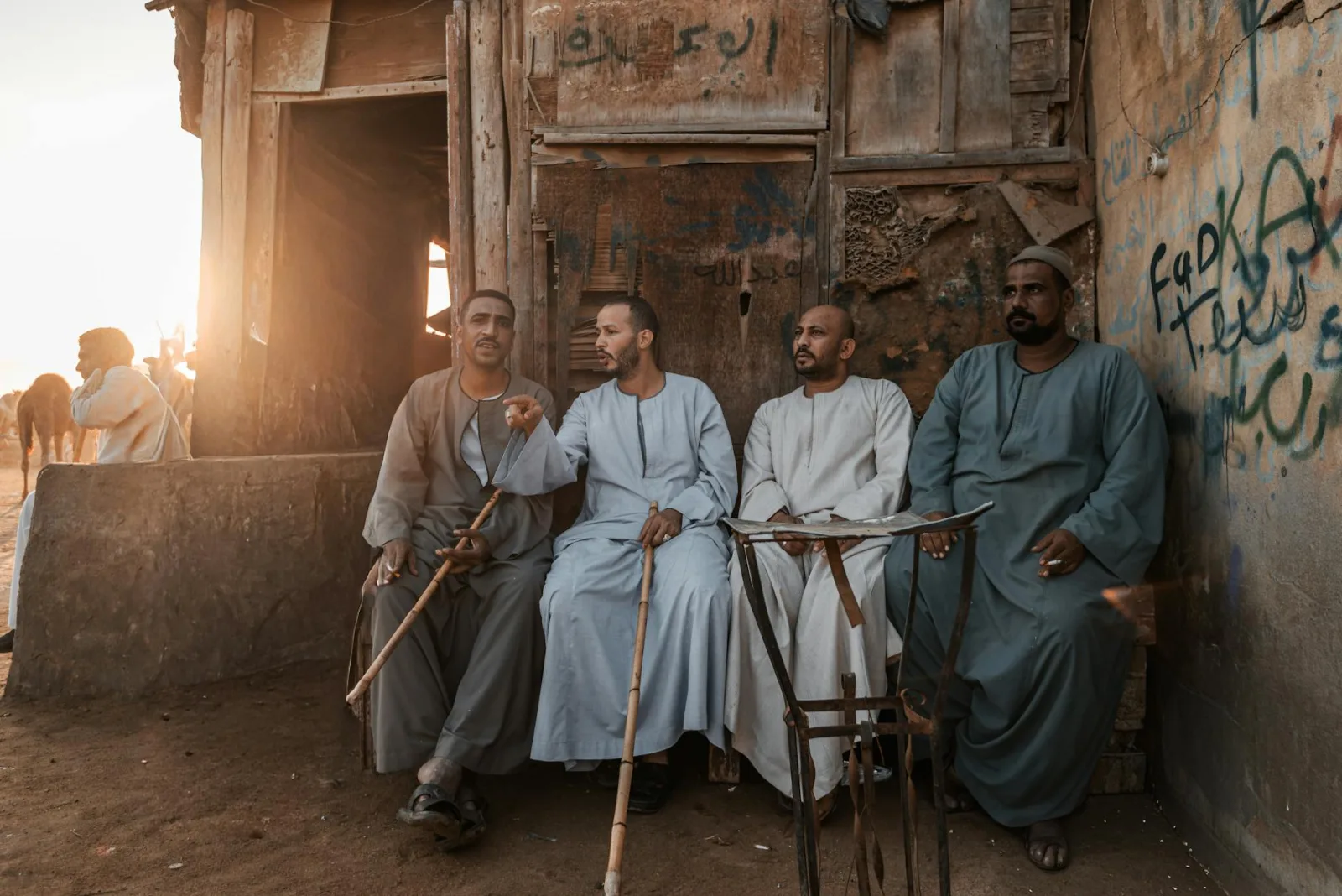 A group of men in traditional clothing sitting outside a rustic building in Egypt during sunset.