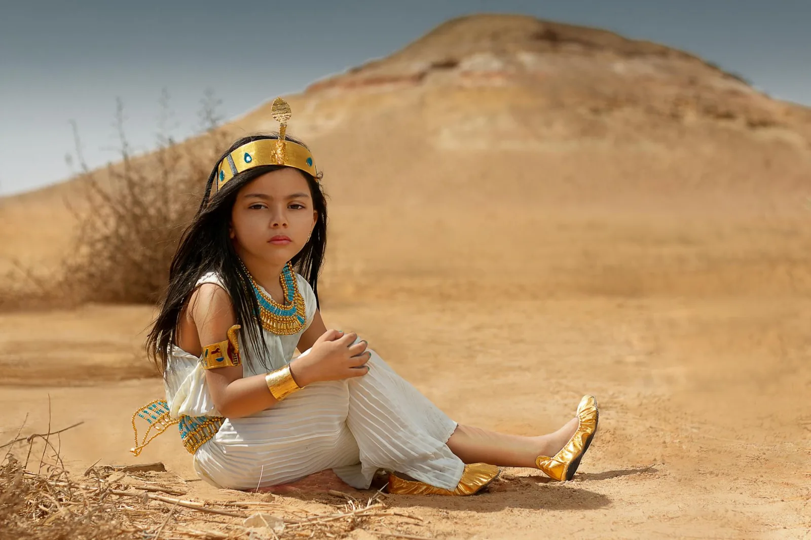 A young girl dressed as an Egyptian princess sitting in a desert landscape.