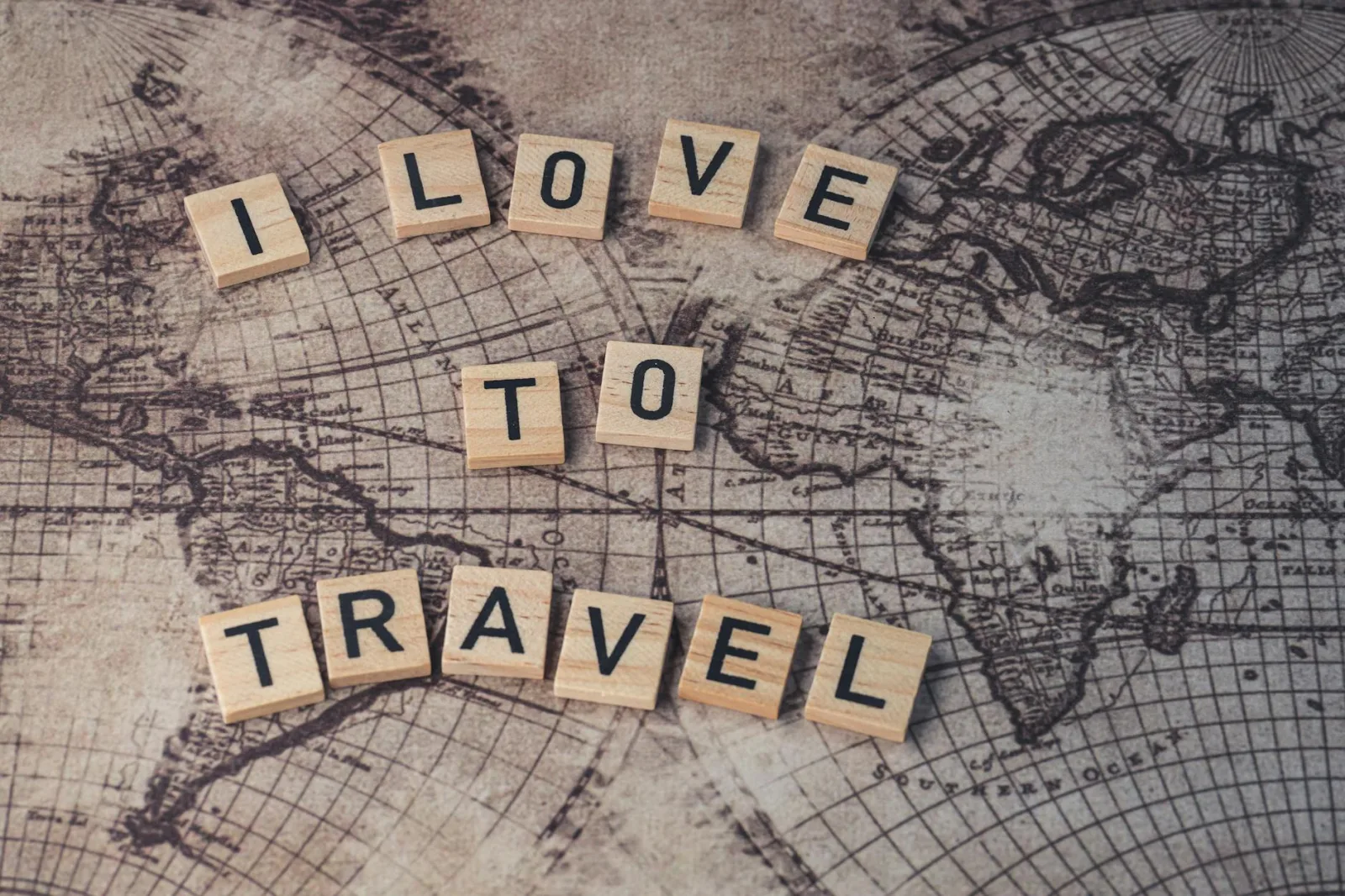 Wood scrabble tiles spelling 'I Love to Travel' on a vintage map.
