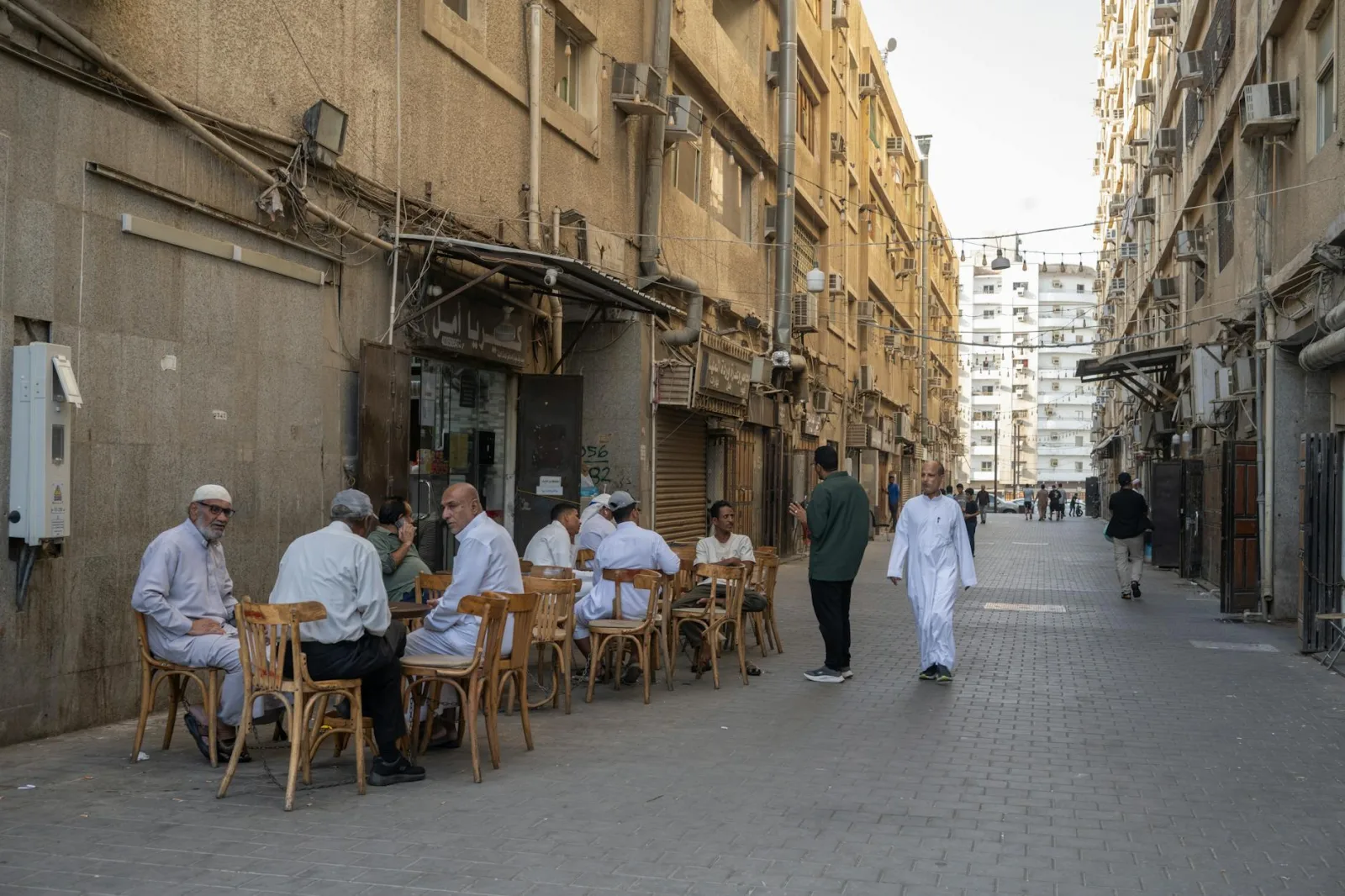 A group of men in traditional clothing sit at tables in an alleyway cafe, showcasing a candid street scene.
