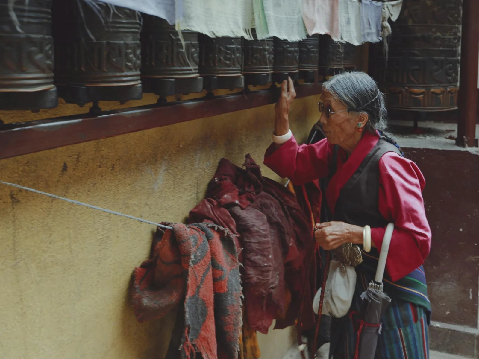Senior woman in traditional attire spinning prayer wheels at a Buddhist temple.