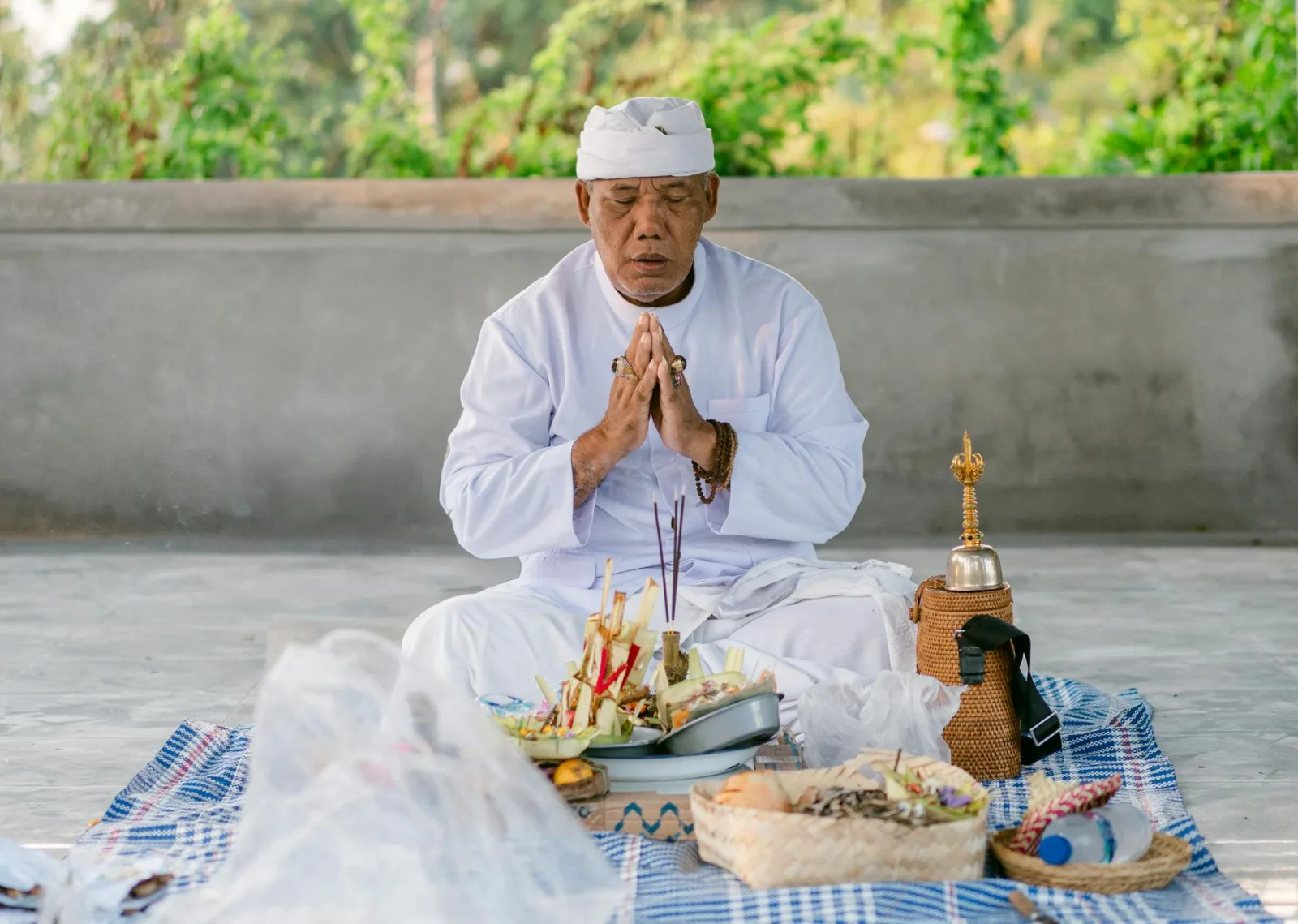 Senior priest in traditional attire performing a prayer ritual outdoors with offerings.