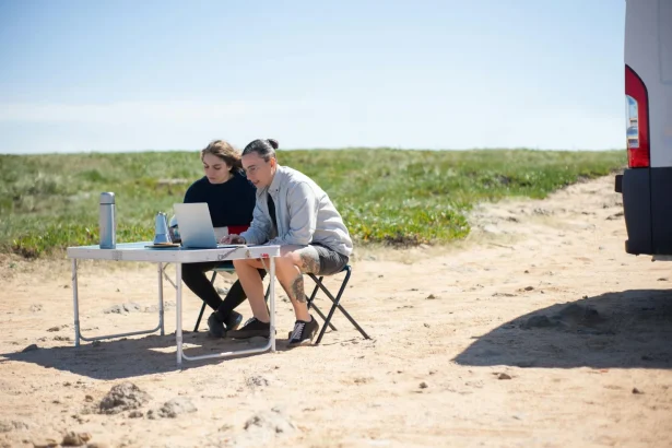 Two adults working on laptops outdoors in Portugal, enjoying a sunny day with portable workspace.