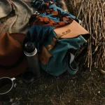 Close-up view of camping essentials including a thermos, backpack, and hat on a blanket.