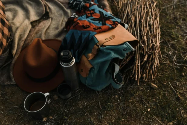 Close-up view of camping essentials including a thermos, backpack, and hat on a blanket.