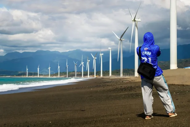 A person photographing the iconic wind turbines at Bangui Wind Farm along the beach in the Ilocos Region, Philippines.
