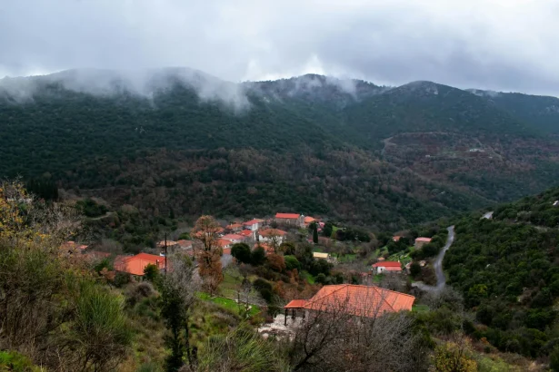Picturesque view of Skliros village nestled in lush Greek mountains under a cloudy sky.