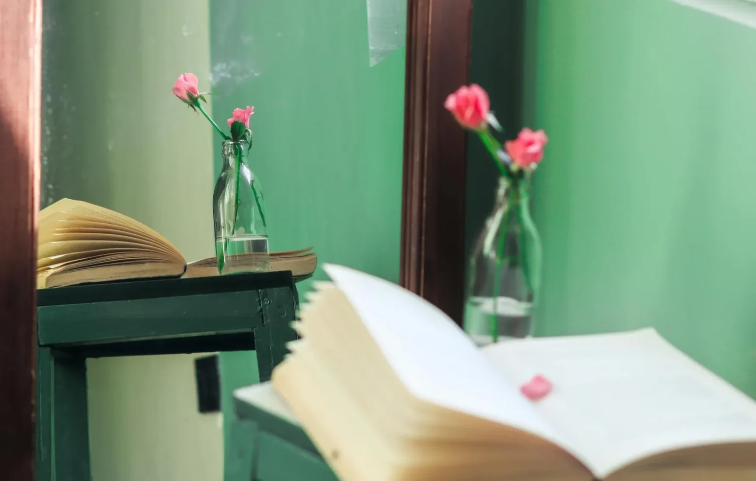 A peaceful reading area with open books and pink flowers reflecting in a mirror.